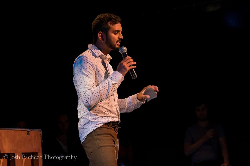 Rohan Bhargava speaking into a microphone and holding a sheet of paper on a stage. 