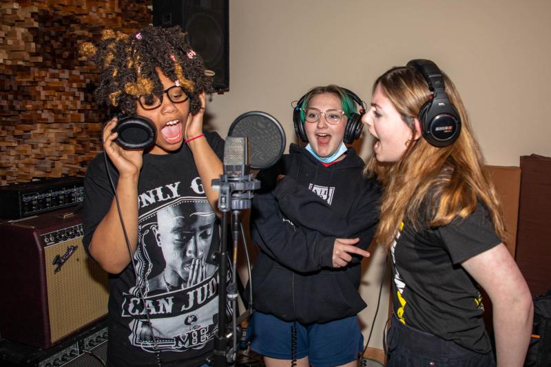 Three teenagers sing around a microphone