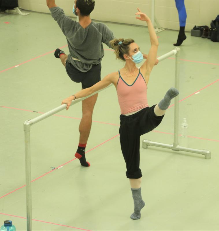 Cincinnati Ballet dance class Two ballet dancers wearing masks lift their legs while rehearsing at the barre