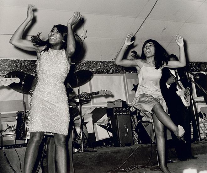 Black and white photo of two women dancing, their hands mid-clap. 