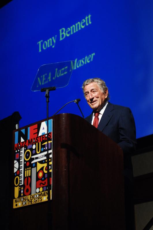 Tony Bennett stands smiling behind a lectern with the NEA Jazz Masters logo