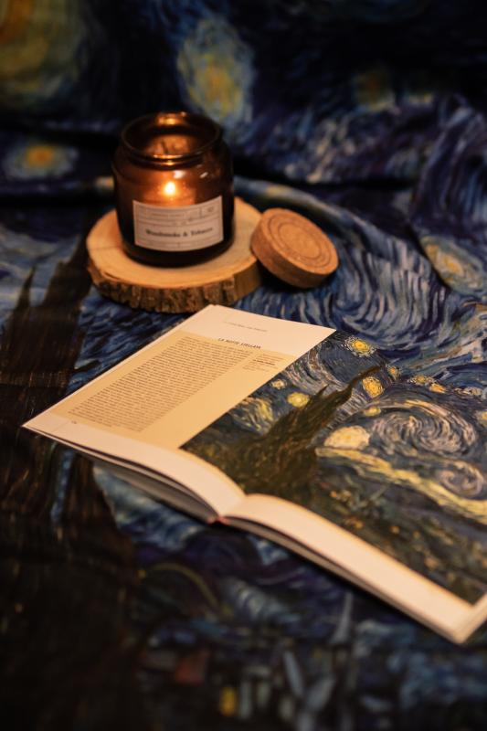 A table cloth of Vincent van Gogh's painting The Starry Night, with a candle on the left and a book of the painting on the right.