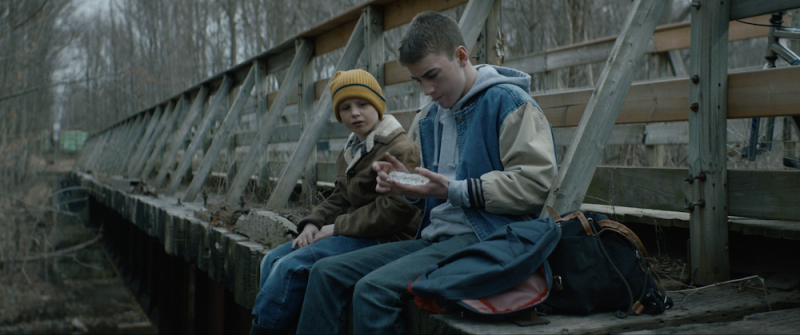 a young boy and a teenage boy sit on the edge of a railroad trestle