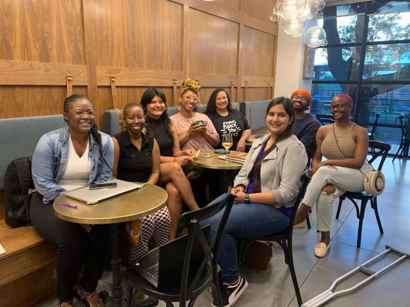 Seven women and one man smiling while sitting at three wooden tables in a restaurant. Seven women and one man smiling while sitting at three wooden tables in a restaurant.