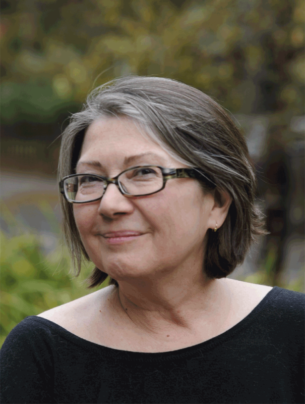 A woman with grey hair and glasses smiles at the camera