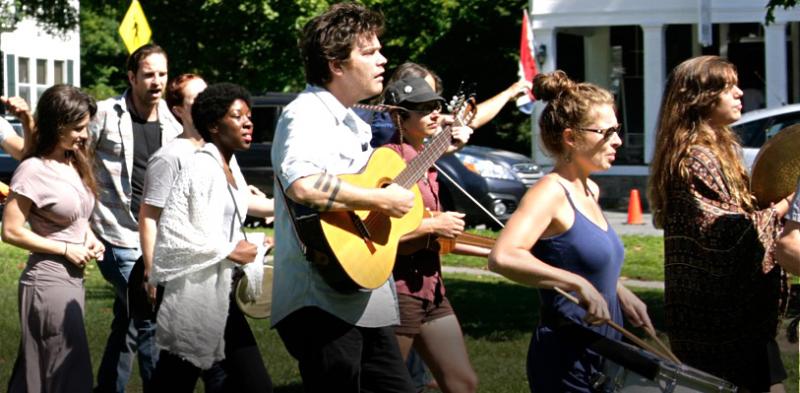 Parade of local townspeople with musicians crossing a neighborhood green