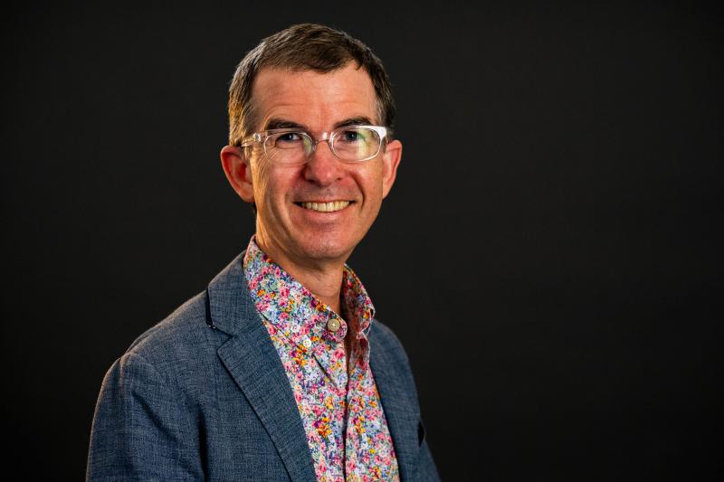 Dalouge Smith, a middle-aged white man with glasses. He is wearing a floral patterened shirt under a medium blue blaxer