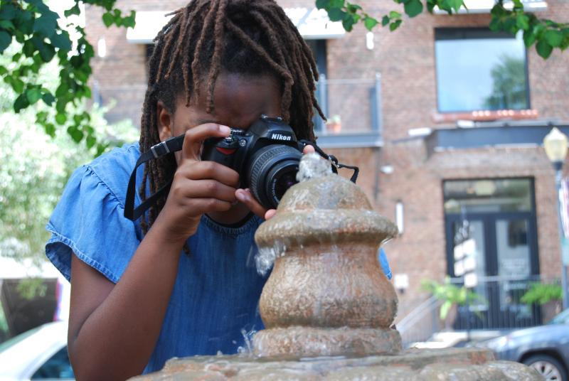 a young girl takes a photo of an object on the street