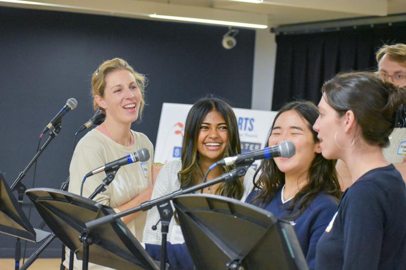 A student stands with performers and her mentor in front of music stand