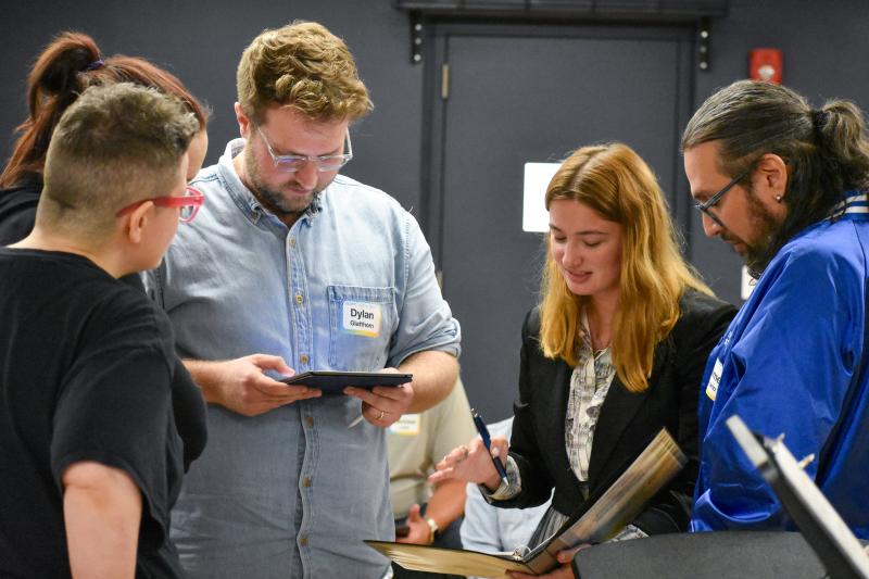A student stands with mentors looking at sheet music