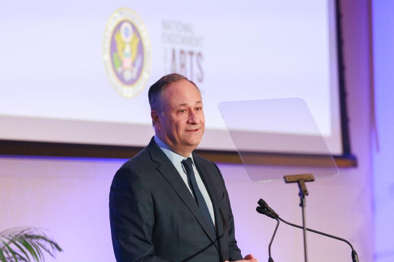 Man with short hair in suit on stage in front of a microphone. 
