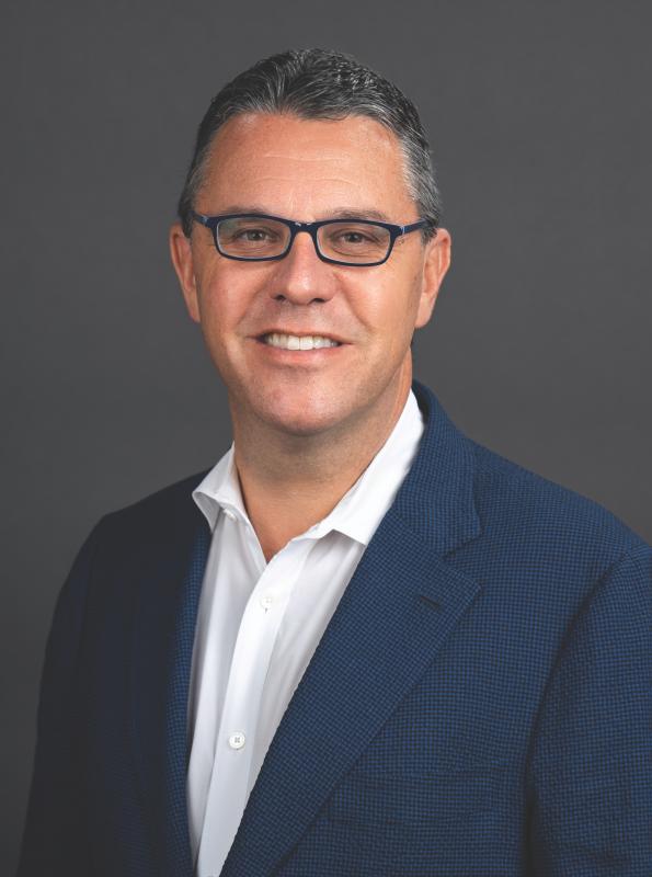 ALT Text: Photo of a White man smiling and wearing glasses and a blue blazer.