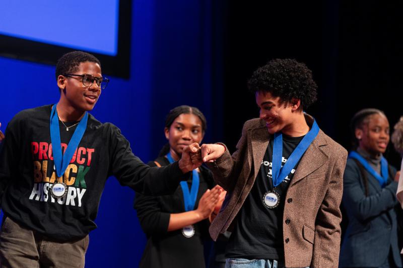Two young men fist pump each other on stage
