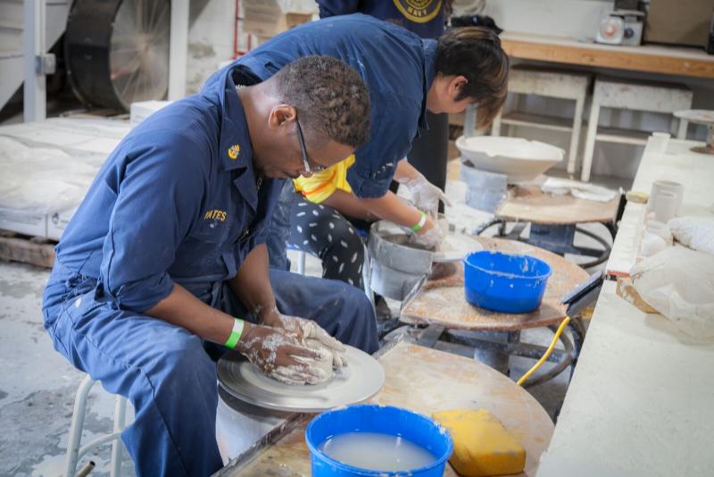 Seated man looks down at clay on a round surface while he works it with his hands