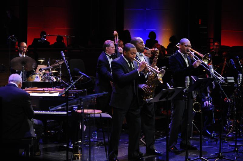 Five Black men and one White man, wearing black suits, perform on stage