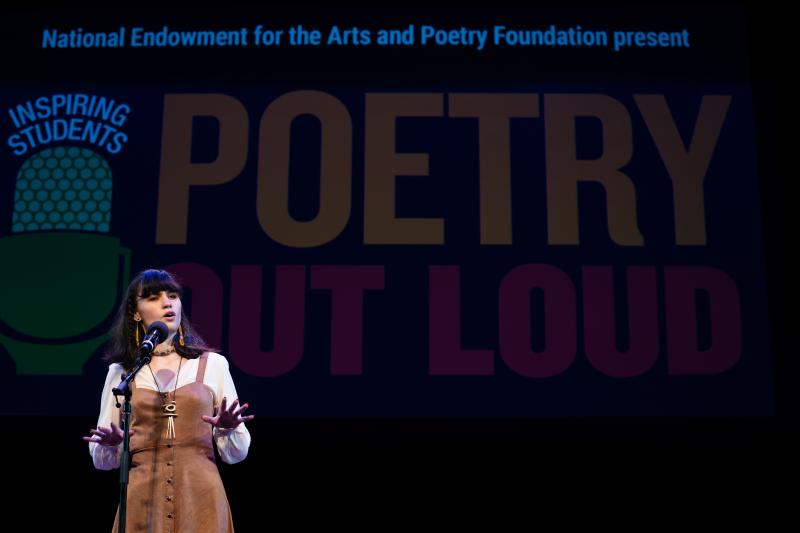 A young Native American woman recites behind a microphone