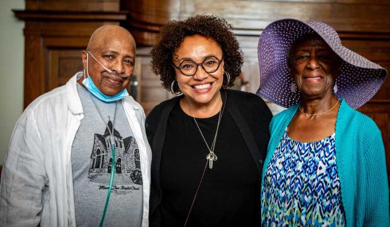 Three women with their arms around one another smile at the camera.