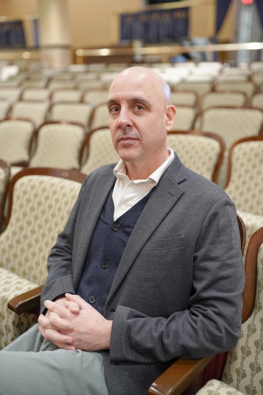 Headshot of a White man seated in an empty auditorium.