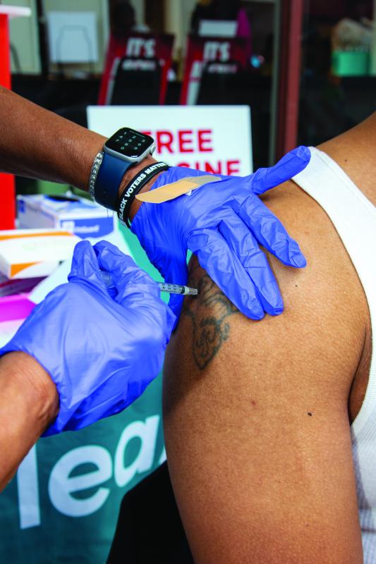 Gloved hands giving a shot to a man's right arm.