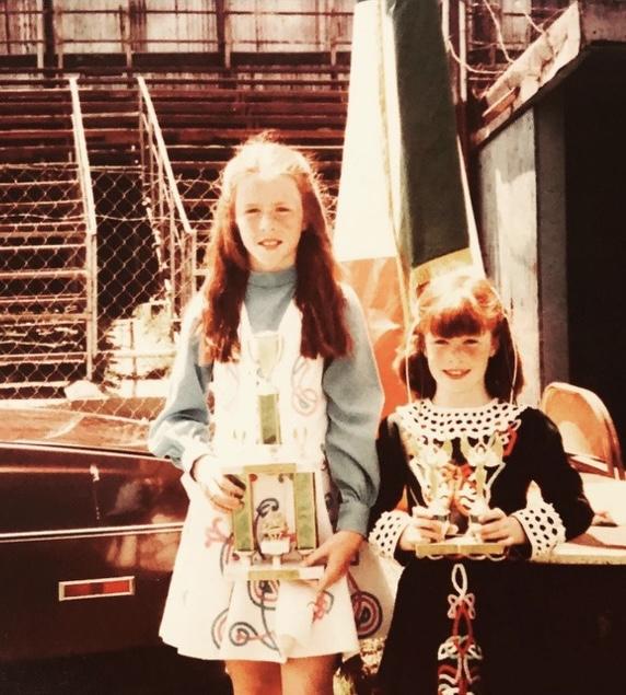 Two young white girls wearing decorative dresses and holding dance trophies.