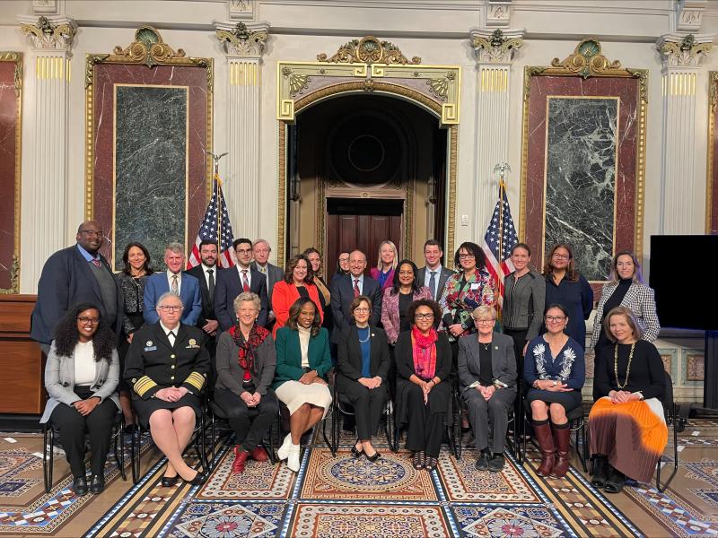 A large group of people pose for a photo in front of two American flags.