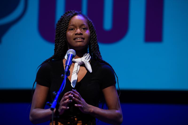 A young Black woman recites behind a microphone