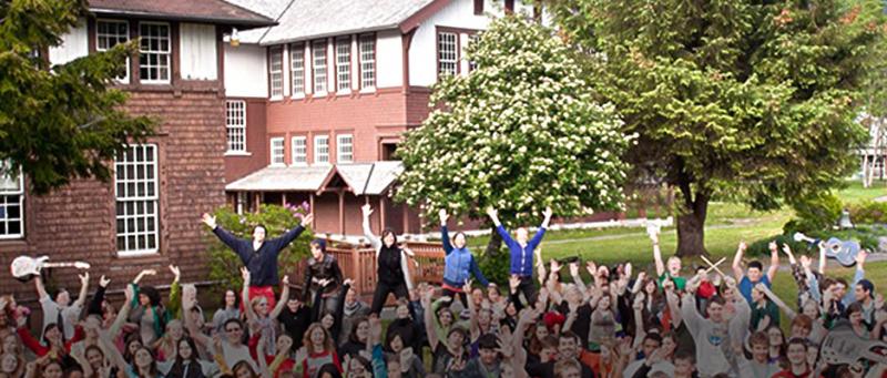 Large group of young people outdoors on a college campus cheering with arms raised