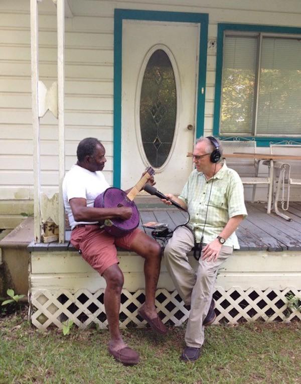 Two men sitting on a porch, one hold a micropone.