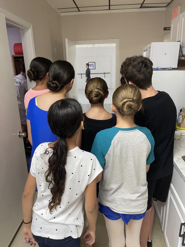 A group of young dancers look through a door to watch a professional dancer rehearse.