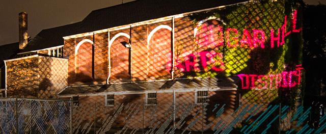 Light projections on a large brick building including the words Sugar Hill Arts District