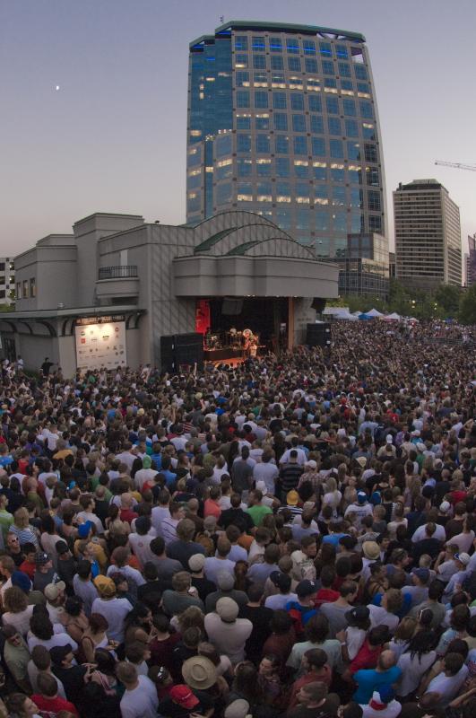 A crowd of people at an outdoor concert in front of large building. 
