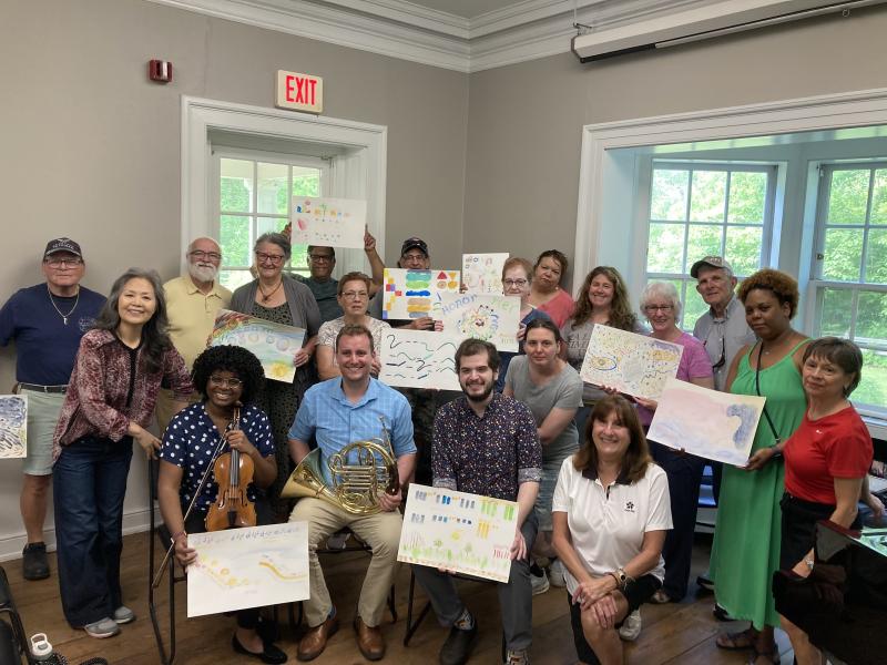 A group of people posing for photo, holding up artwork they have done.