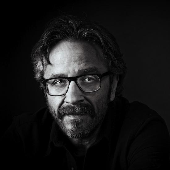 close-up of a white man with glasses and salt and pepper hair against a black background