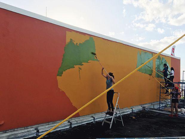 Teenagers stand on ladders and paint a mural using paint rollers