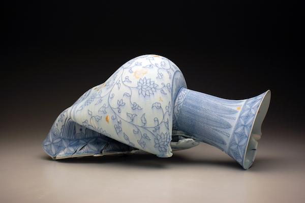 a blue and white vase that appears broken and cracked at the edges lying on its side