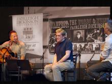 Musician Bruce Springsteen laughs as he reacts to poet Robert Pinsky and author Wesley Stace on stage at the Words and Music Festival, 2010.  The backdrop is a WAMFEST poster with images of participating artists.