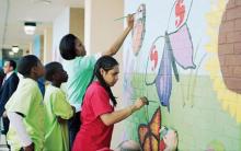 Michelle Obama and young African American students painting a mural on a brick wall