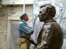 an older African American man stands face to face with a very large size bronze sculpture of Abraham Lincoln