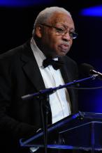 A man in a tuxedo speaks at a podium