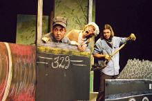 young actors in a cardboard locomotive mock-up with  another shoveling pretend coal into the firebox.