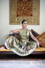 A woman in classical Indian dress seated amongst colorful pillows strikes the pose of the goddess Devi