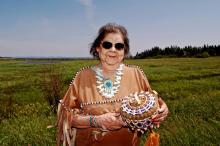 Woman in traditional dress holding a woven basket and standing in a large field.