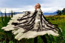 A woman stands in a field twirling while wearing a black and white woven robe.