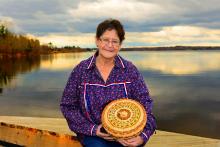 A woman stands in front of water, holding a woven basket