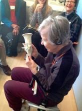 An older woman sits in a chair and holds a small sculpture. 