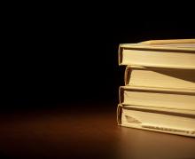 Four books stacked on top of each other. They are sitting on a empty table. 