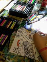 A pair of hands use a variety of markers to create a picture