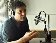 Abbas Raza with headphones and speaking into a microphone.
