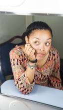 A young black woman looks sideways and is reflected in a dressing room mirror