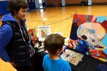 A woman artist talks to a young boy as he looks at one of her paintings provided by Art Mobile of Montana